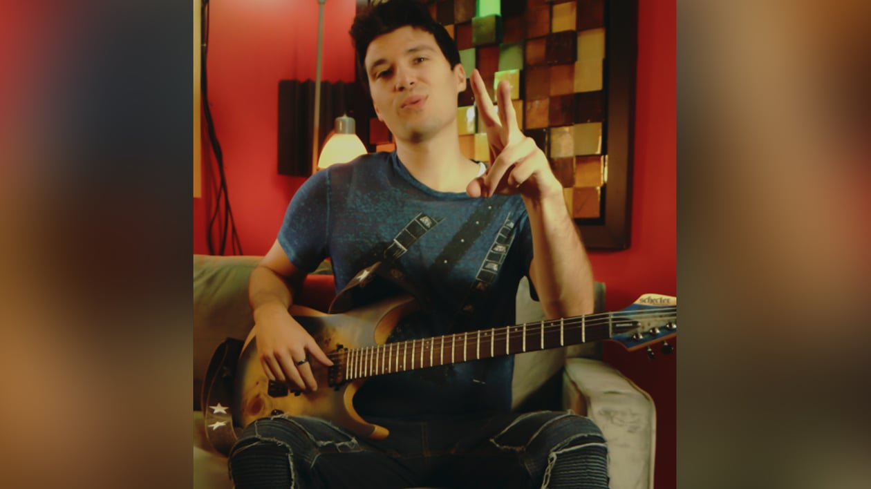 Frank Palangi in a red room on a chair with a guitar on his lap