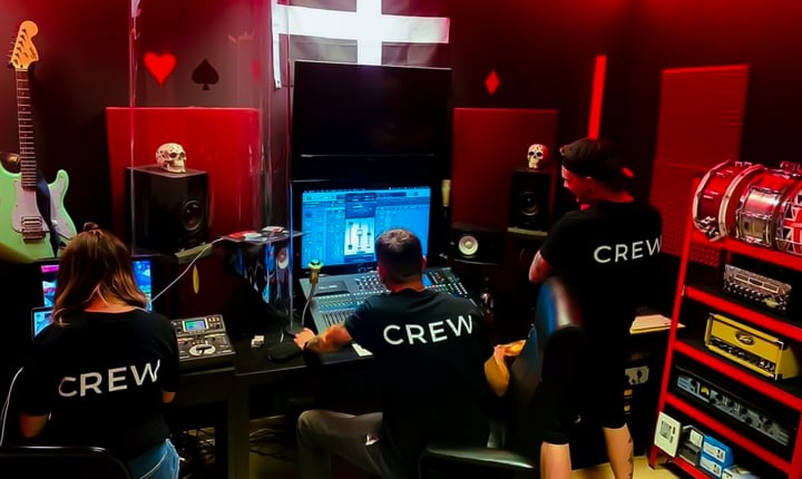 Recording studio photo in the control room. Three members of Card Trick Studios working on a studio desk with "crew" shirts on and a red hue in the room.
