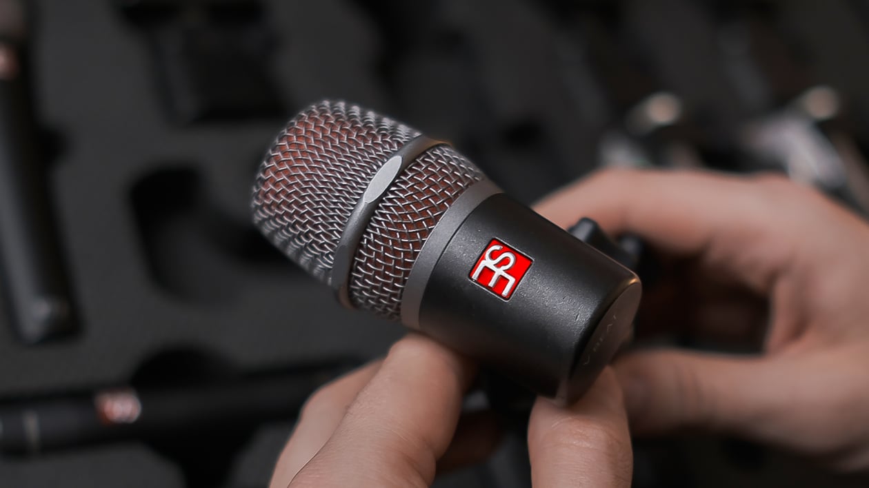 Close-up of Maxim Moskovkin holding a dark gray V Beat microphone with an open mic case blurred in the background.