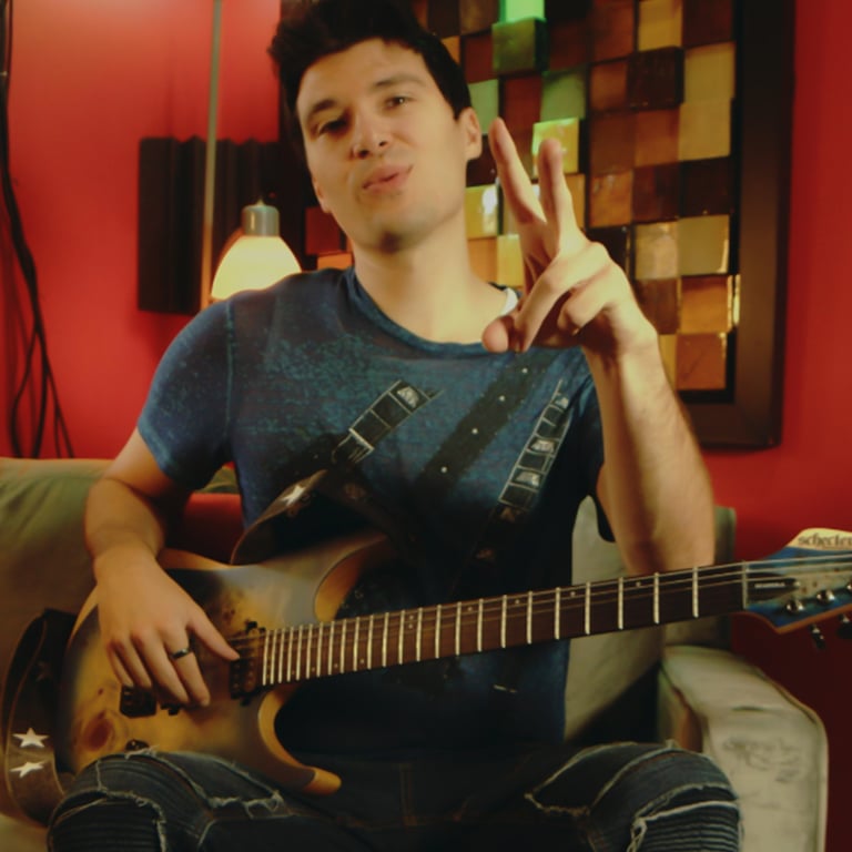 Frank Palangi in a red room on a chair with a guitar on his lap