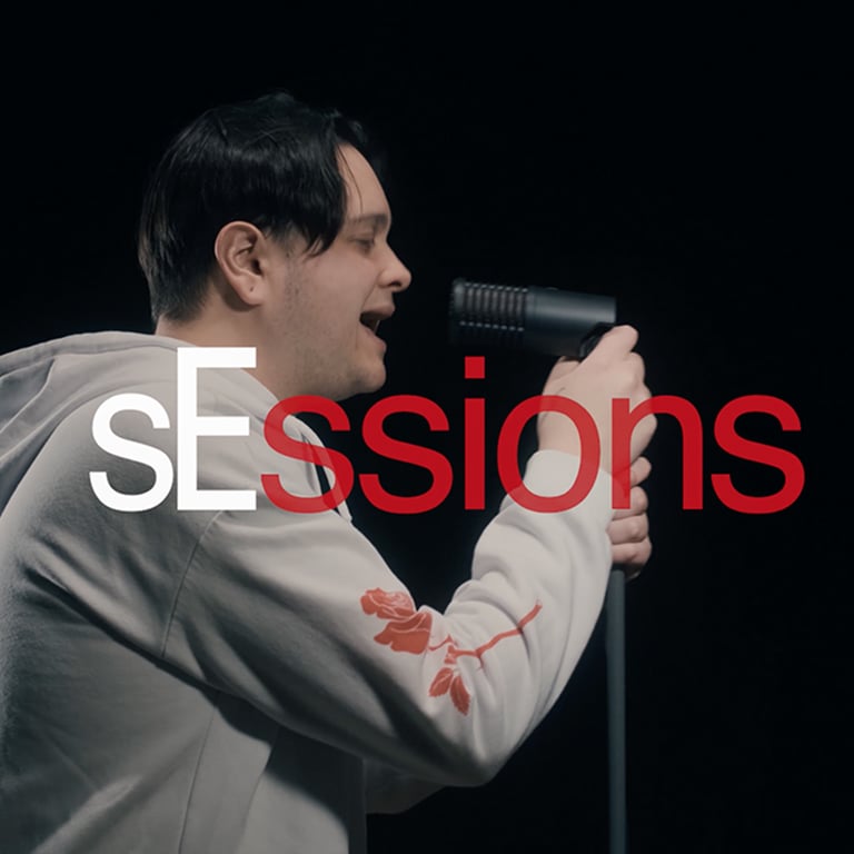 sEssions text with white "sE" text and red "ssions" text. A male with black hair singing into a DynaCaster microphone matte black with red showing through the metal mesh grille.