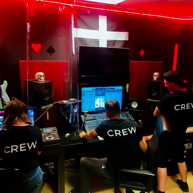 Recording studio photo in the control room. Three members of Card Trick Studios working on a studio desk with "crew" shirts on and a red hue in the room.