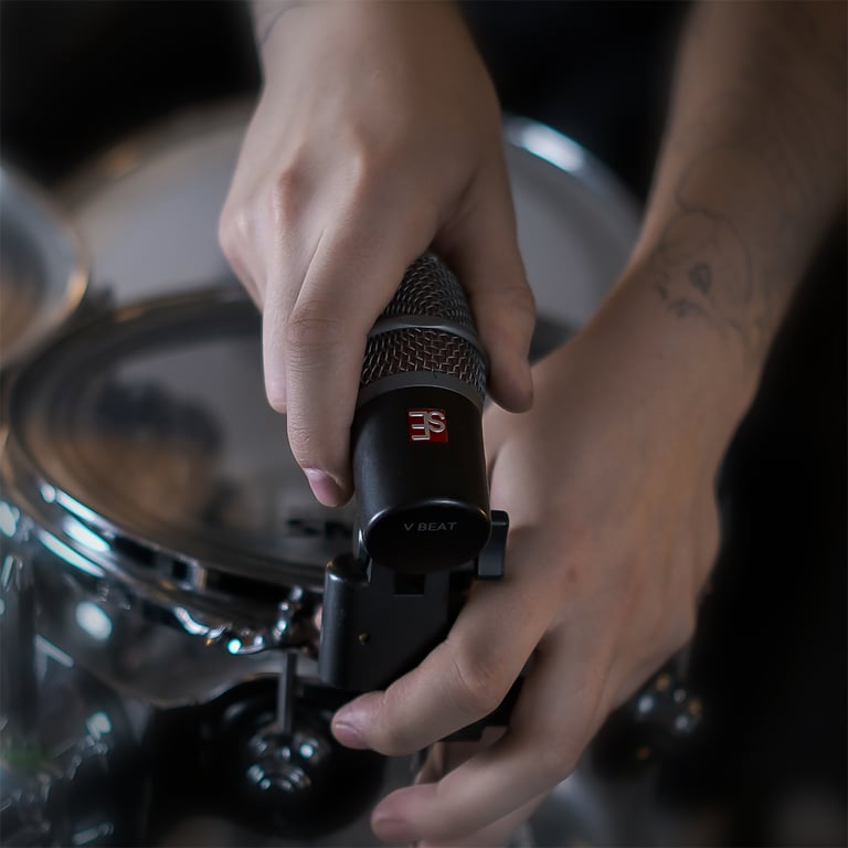 Close up of Maxim Moskovkin clamping a dark gray V Beat microphone with the V Clamp to the rim of a tom.