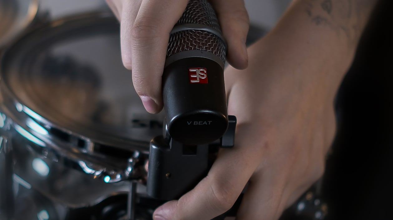 Close up of Maxim Moskovkin clamping a dark gray V Beat microphone with the V Clamp to the rim of a tom.