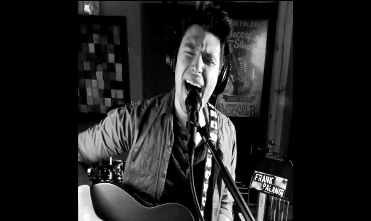 Black and white photo of a singer with an acoustic guitar in a cluttered studio room