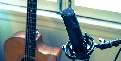 The sE2200 studio condenser microphone in a recording setting pointed towards a Taylor acoustic guitar that is leaning on a window frame.