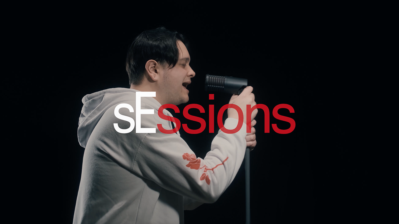 sEssions text with white "sE" text and red "ssions" text. A male with black hair singing into a DynaCaster microphone matte black with red showing through the metal mesh grille.