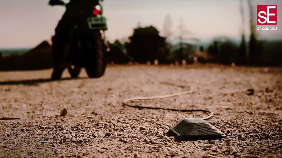 The BL8 tied to a rope that is attached to a dirt bike on a gravel road with trees and power lines in the background.