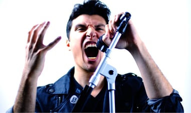 Frank Palangi with a white background screaming into a V7 microphone. There is a microphone stand in the image with a blue hue.