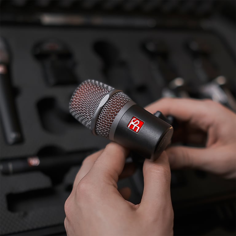 Close-up of Maxim Moskovkin holding a dark gray V Beat microphone with an open mic case blurred in the background.